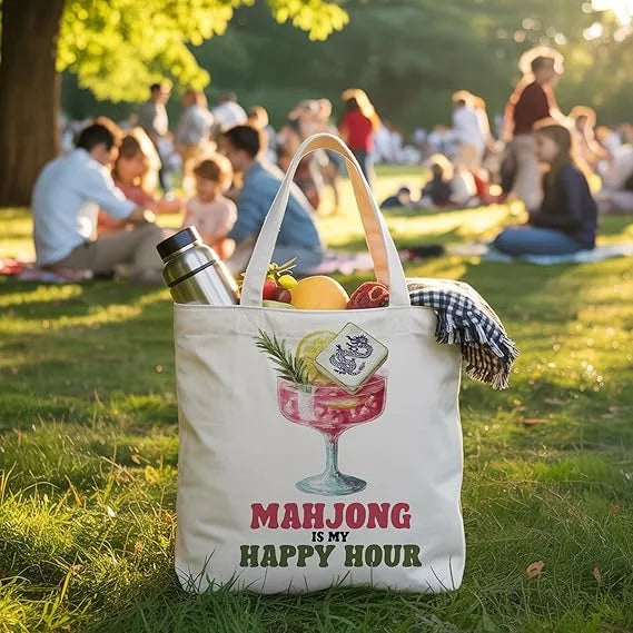 Cotton happy hour tote on the grass at a picnic, filled with fruit, a bottle and a checked blanket
