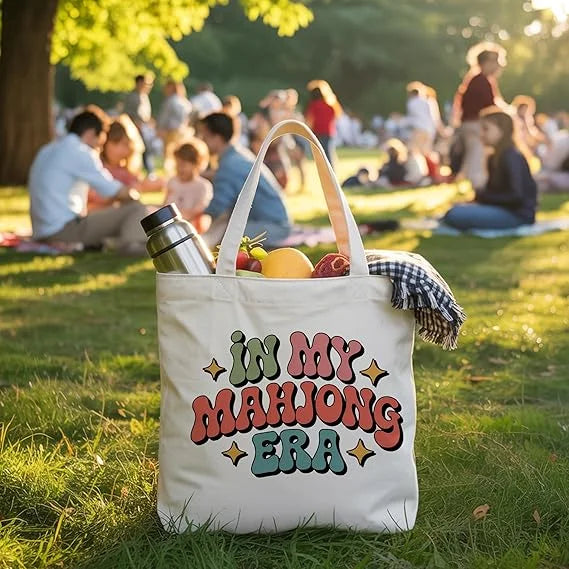 Cotton tote in the In My Mahjong Era print at a picnic, holding fruit, a bottle and a blanket