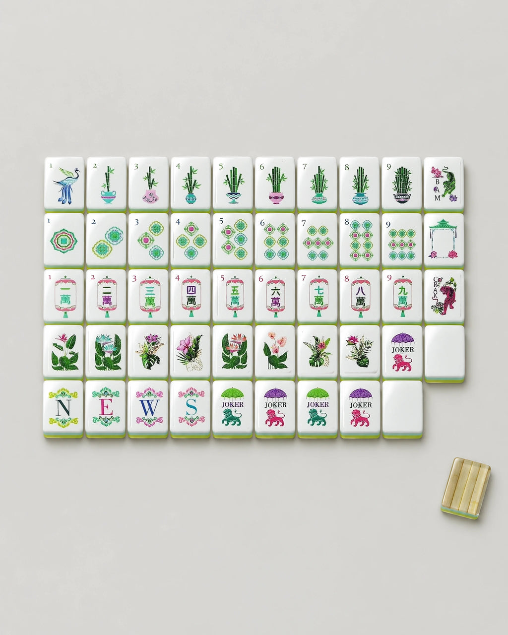 Monstera bamboo mahjong tiles laid out face up, showing every dot, potted bamboo bam, lantern crak, wind, tiger dragon, tropical flower, both joker designs and a blank beside one clear bamboo-inlay back
