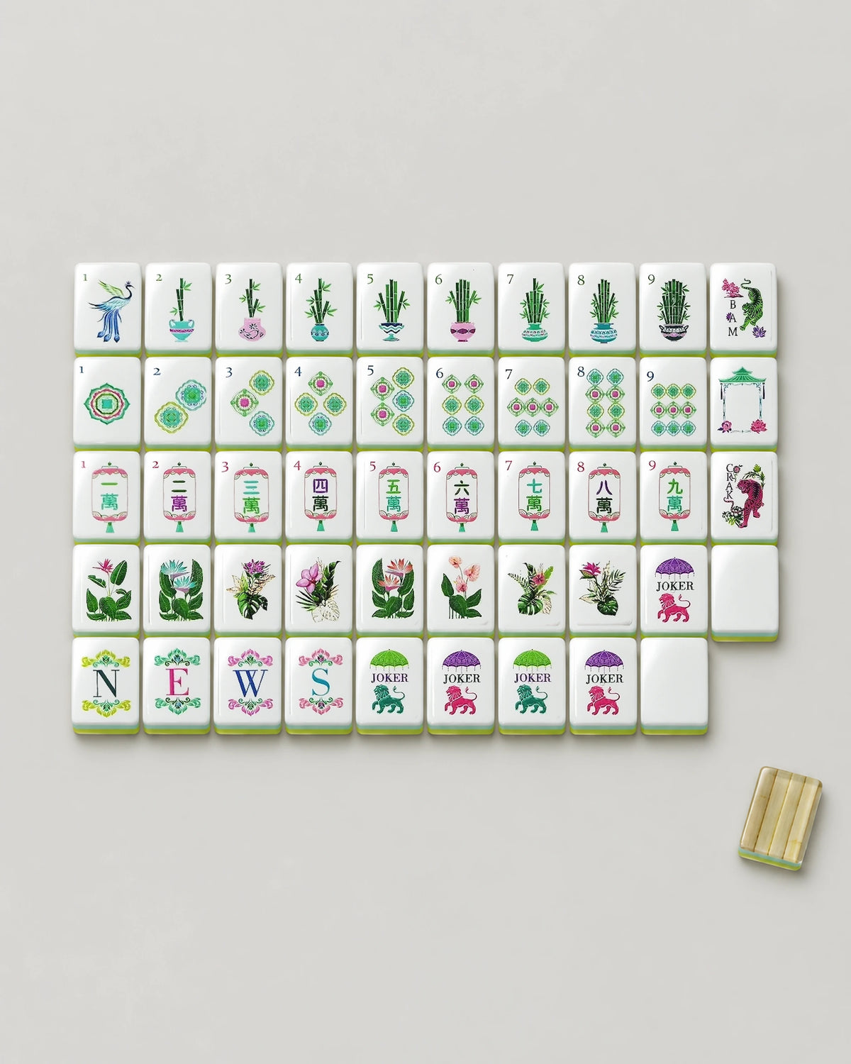 Monstera bamboo mahjong tiles laid out face up, showing every dot, potted bamboo bam, lantern crak, wind, tiger dragon, tropical flower, both joker designs and a blank beside one clear bamboo-inlay back