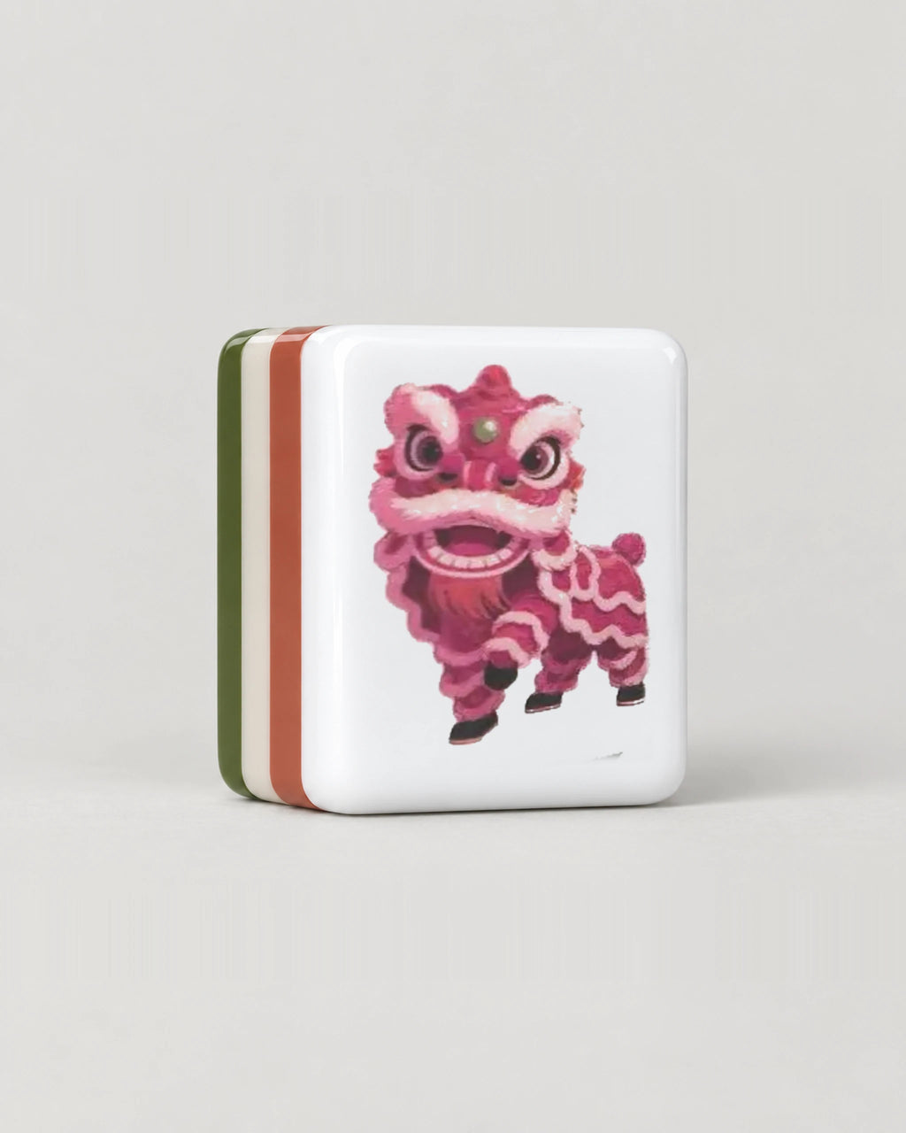 Close-up of one Olivine olive green mahjong tile, the pink-red lion dance dragon, showing its white face and the colored layers along its edge