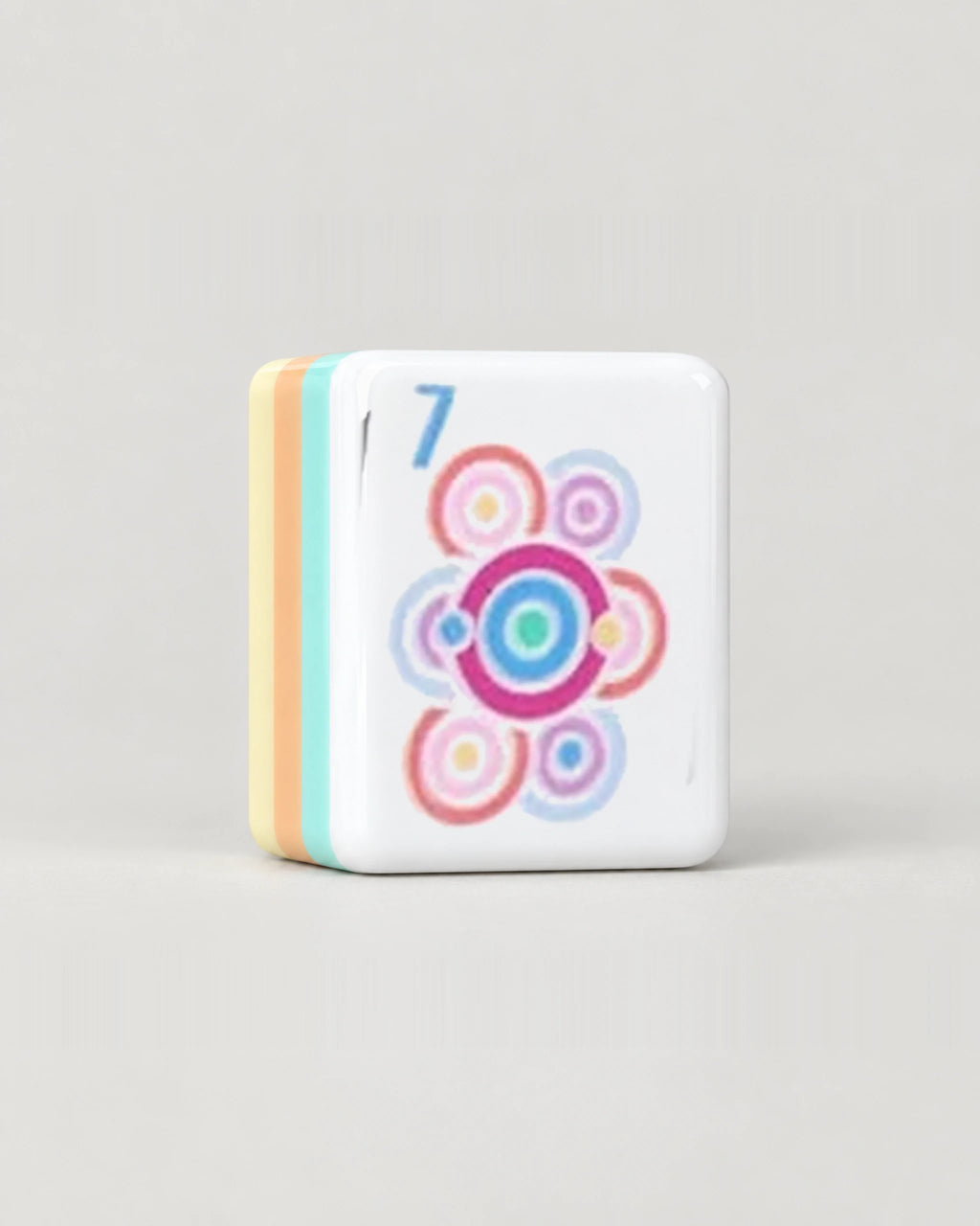 Close-up of one Sherbet pastel mahjong tile, the 7 Dot with concentric rings, showing its white face and the mint, peach and butter yellow layers along its edge