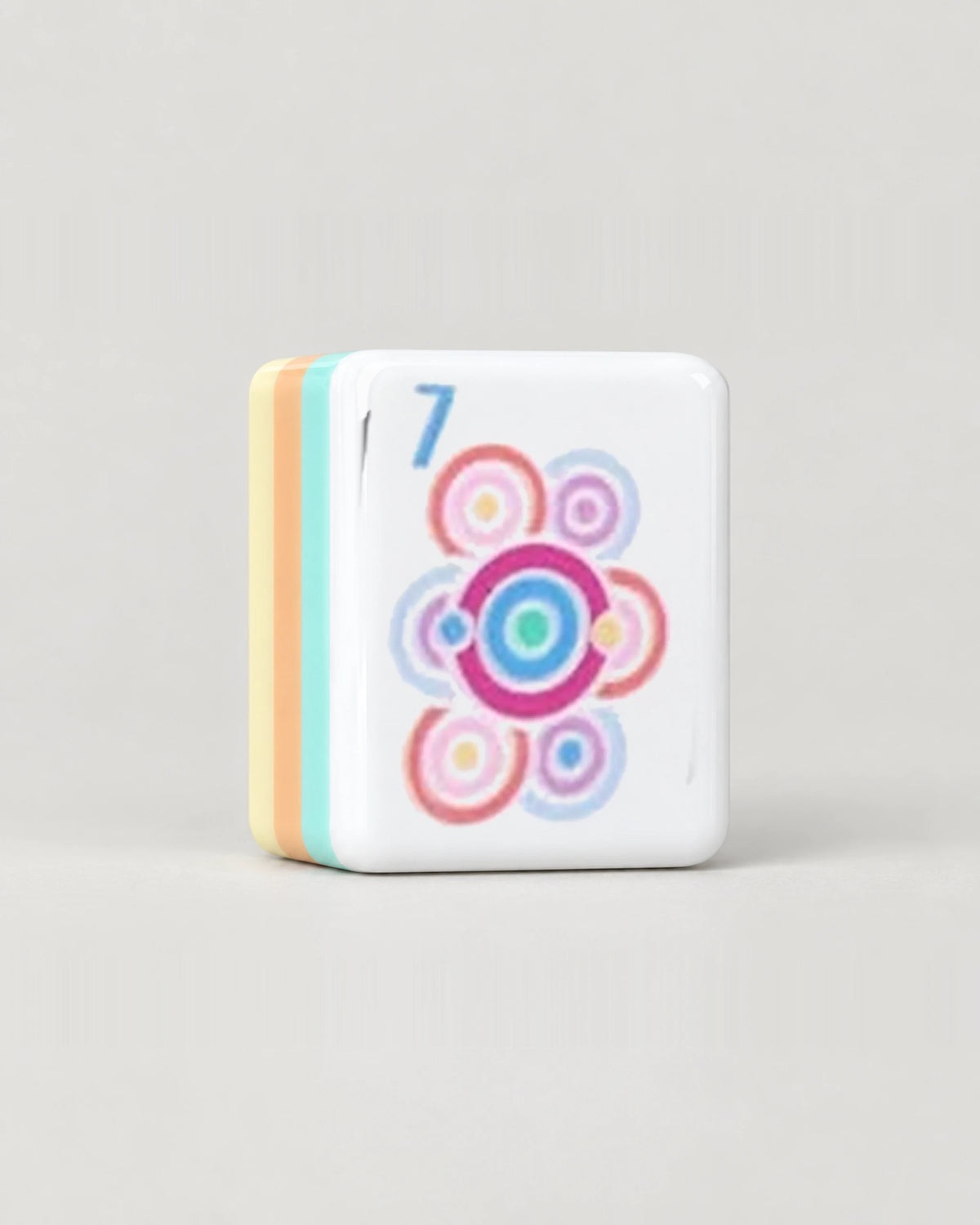 Close-up of one Sherbet pastel mahjong tile, the 7 Dot with concentric rings, showing its white face and the mint, peach and butter yellow layers along its edge