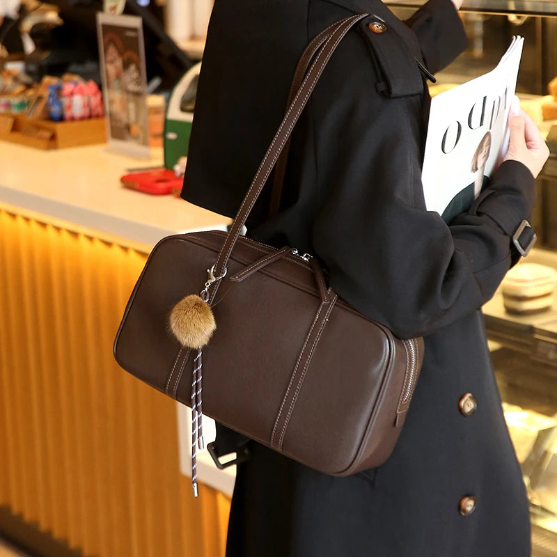 Teak in brown on the shoulder in a cafe, its long straps resting over a black wool coat